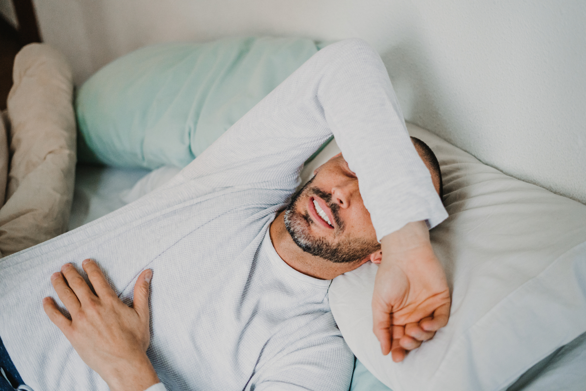 Man Lays in Bed With Arm Draped Across his Face