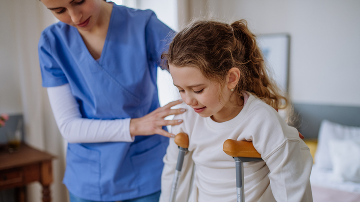 Young nurse helping to walk to little girl with broken leg