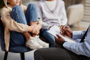 Doctor writes notes on clipboard as young girl speaks in background