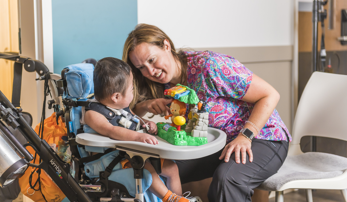 female care worker smiles at a small toddler in a wheelchair