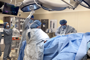 four masked and gowned care providers work on a patient in an operating room