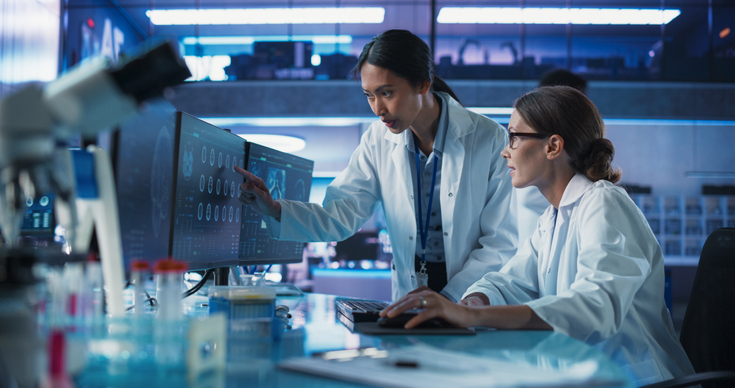 Two female scientists collaborating in a medical research lab while analyzing a brain scan on a desktop computer.