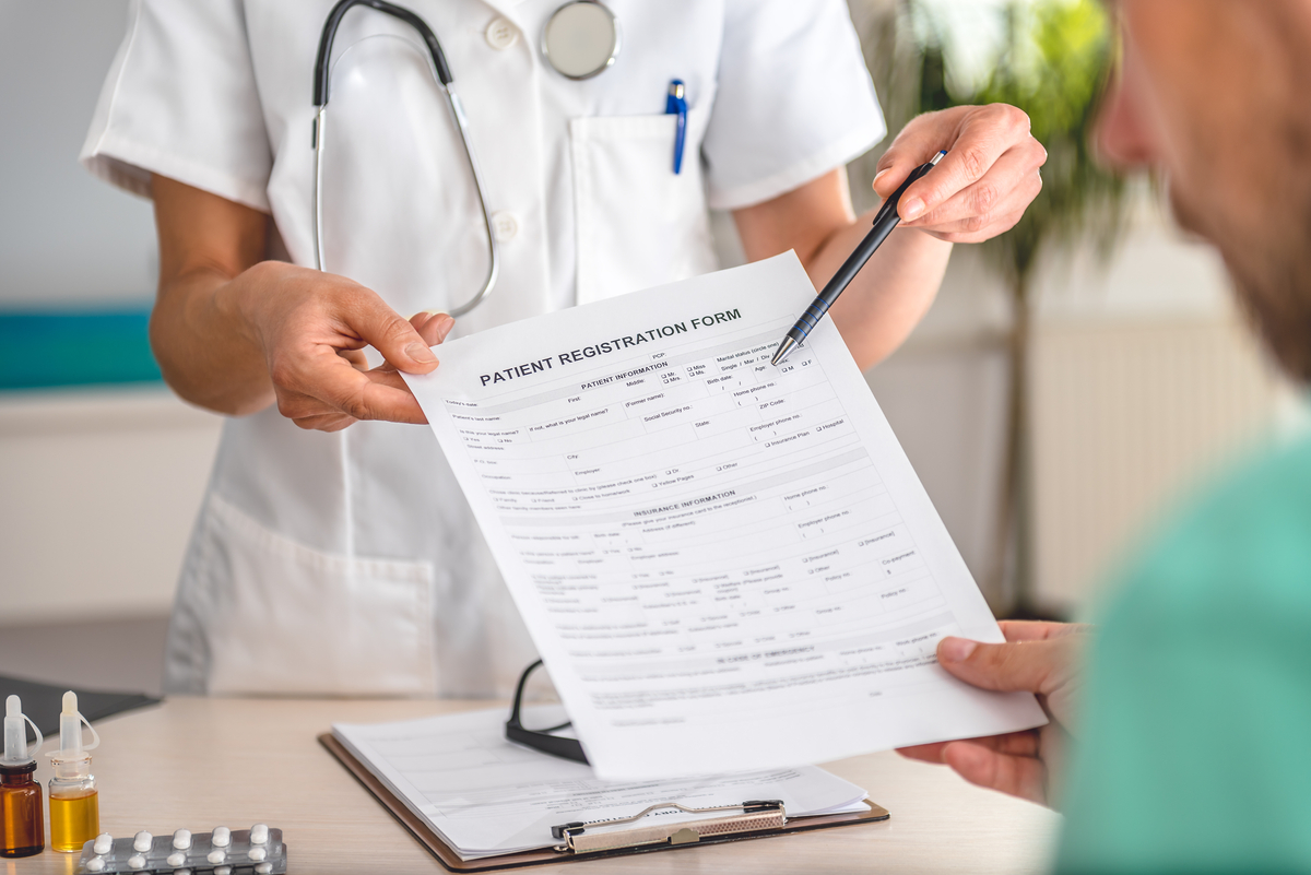 Provider Holds a Patient Registration Form with a Pen