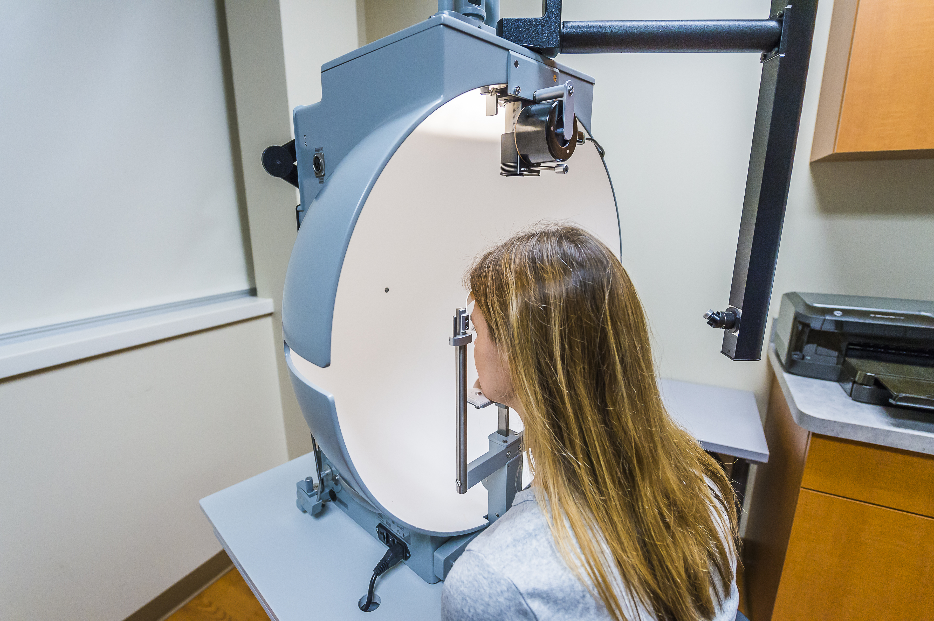 A woman undergoing an ophthalmic examination using specialized equipment in a clinical setting.