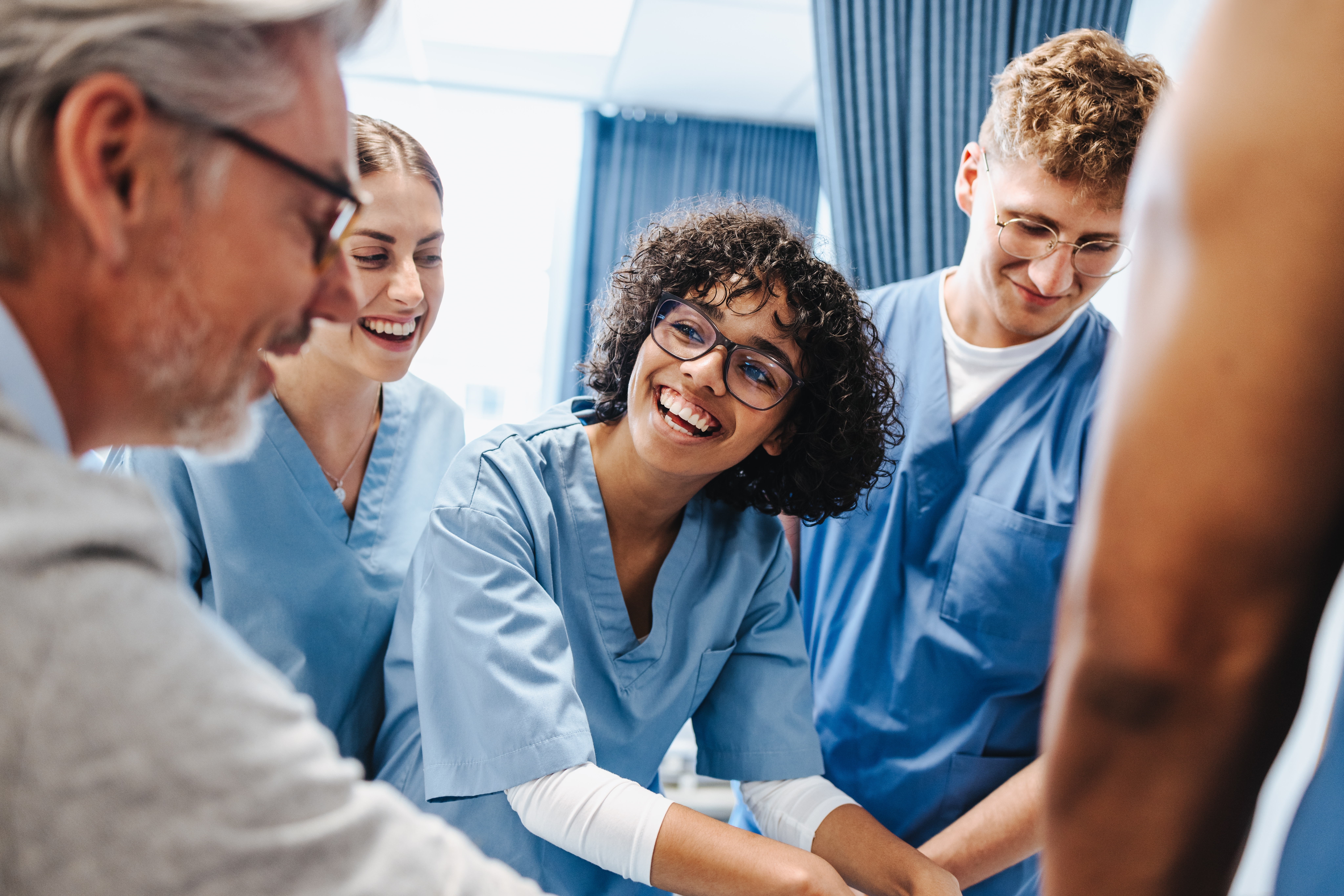 Group of healthcare professionals in scrubs smiling and assisting a person in a medical setting.
