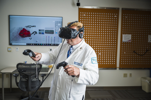 male in lab coat and VR headset holds VR controllers in each hand