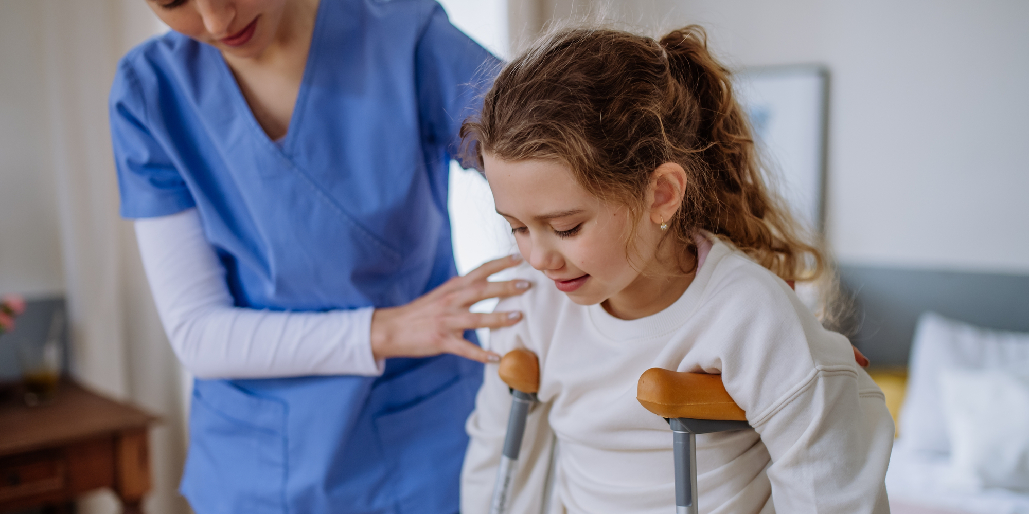 Young nurse helping to walk to little girl with broken leg