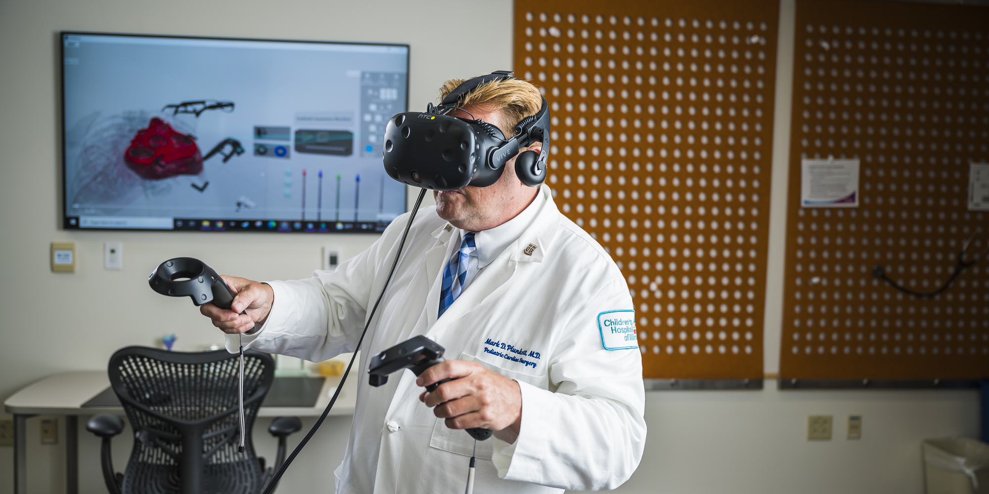 male in lab coat and VR headset holds VR controllers in each hand