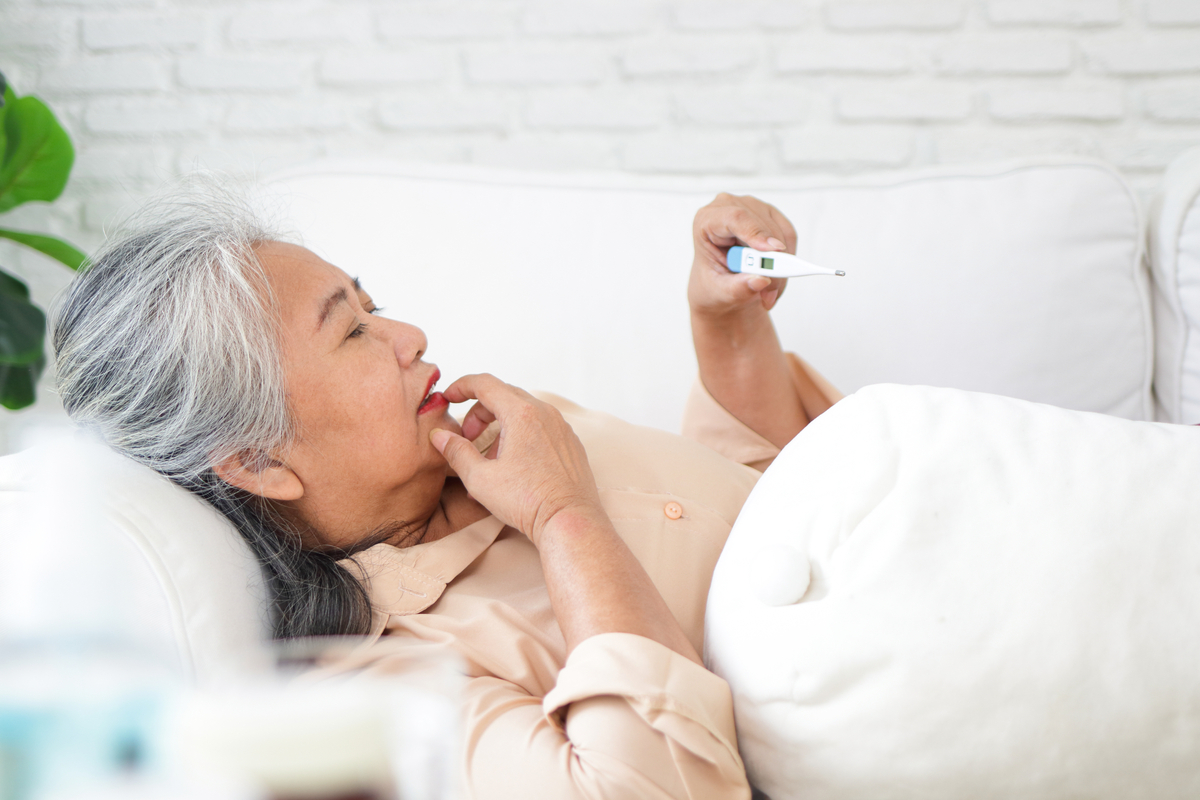 Senior Woman Lay in Bed Holding Up a Thermometer 