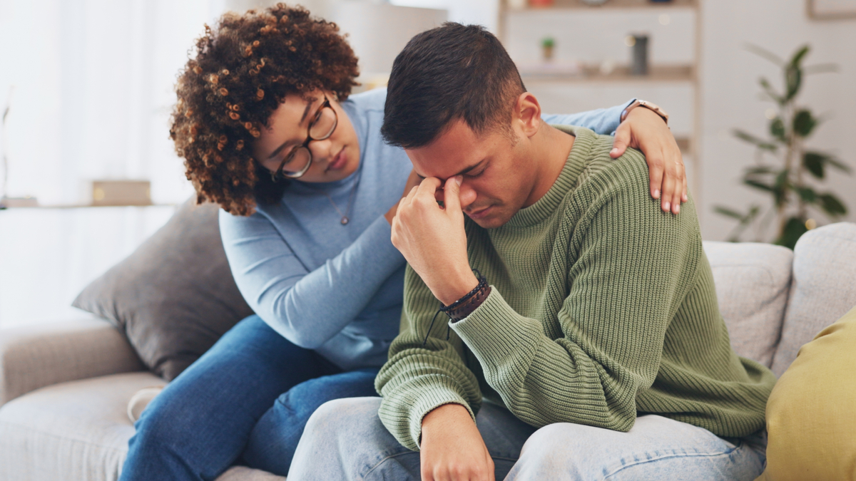 Woman comforting a sad man on the couch