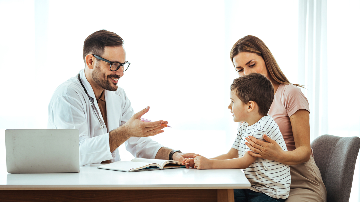 Doctor smiling and sitting while talking to a young boy and his mom