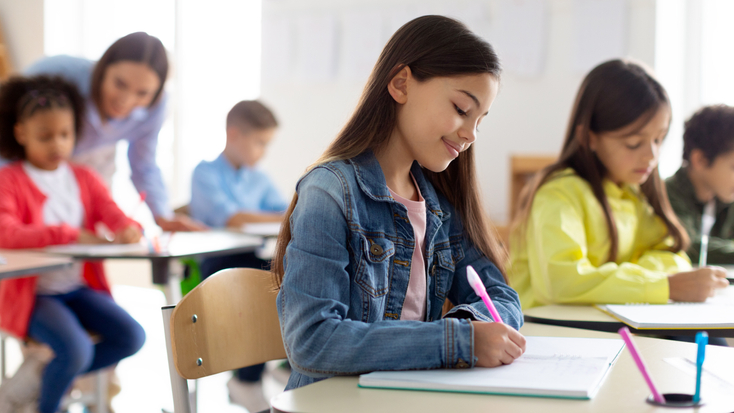 A group of elementary school students sitting at their desks and focused on writing in their notebooks.