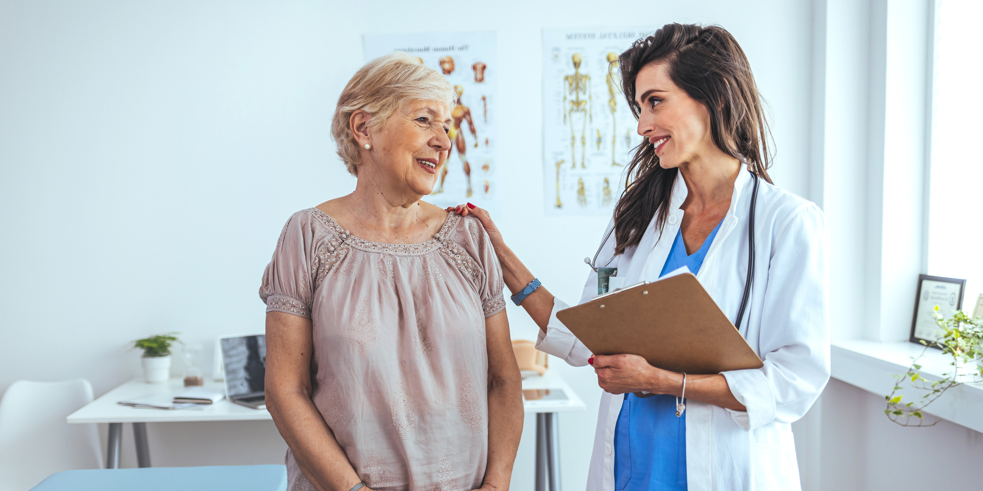 senior patient smiles next to a young female doctor with her hand on her shoulder