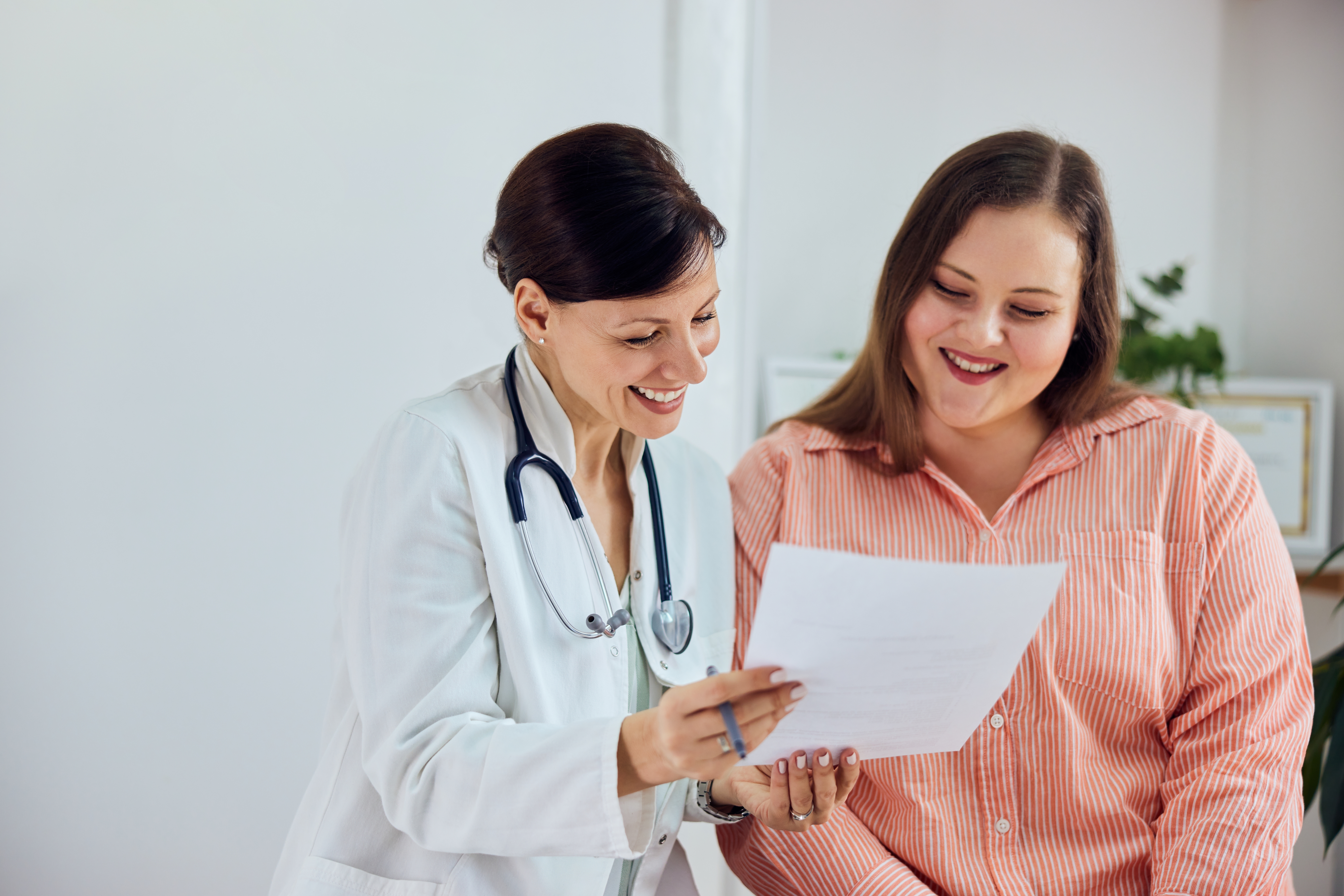 A doctor and a patient smiling while reviewing a document together in a bright medical office.