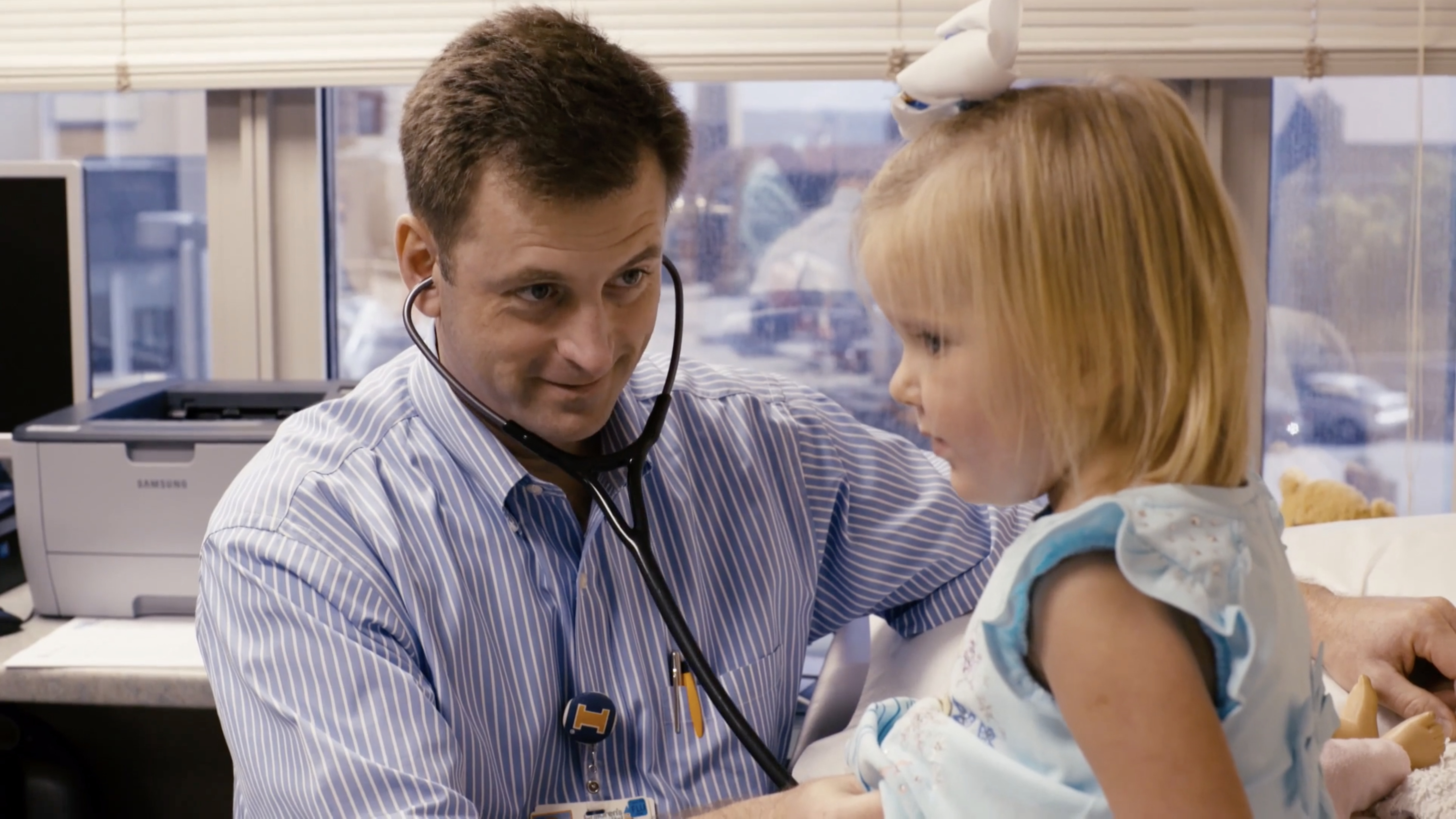 A doctor listens to a young girl's chest with a stethoscope in a medical office setting.