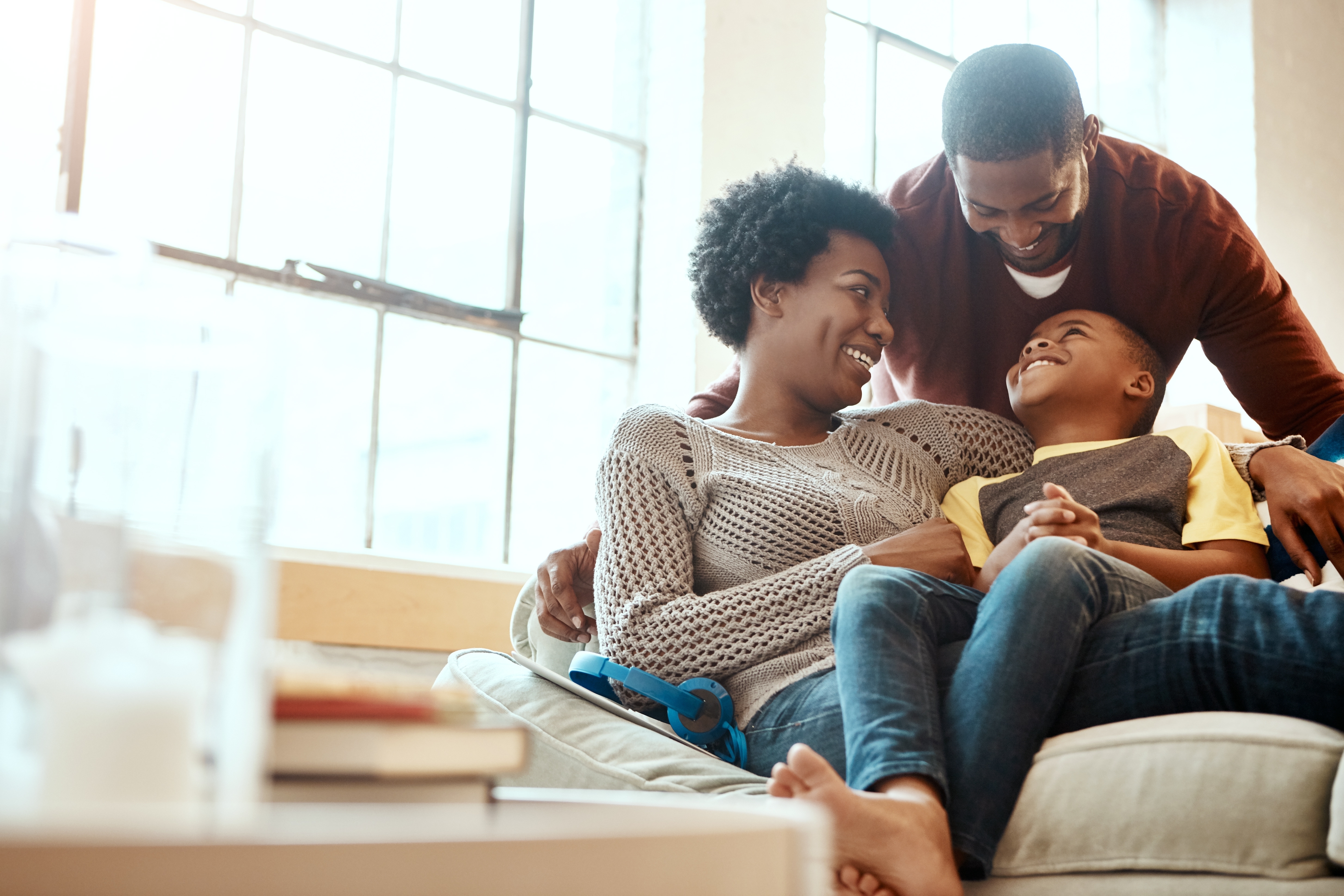 A family of three smiling and sitting together in a bright room.