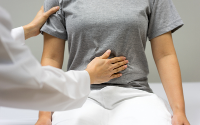 A healthcare professional in a white coat gently placing a hand on a patient's abdomen during a medical examination.
