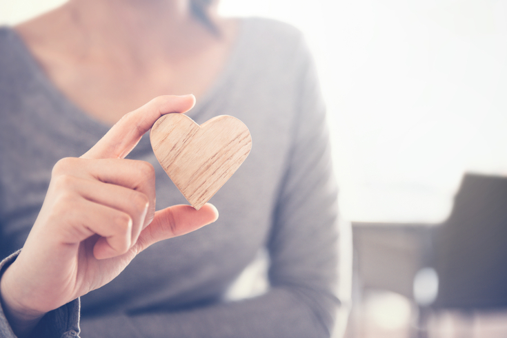 A hand holding a wooden heart shape against a blurred background with ample copy space.