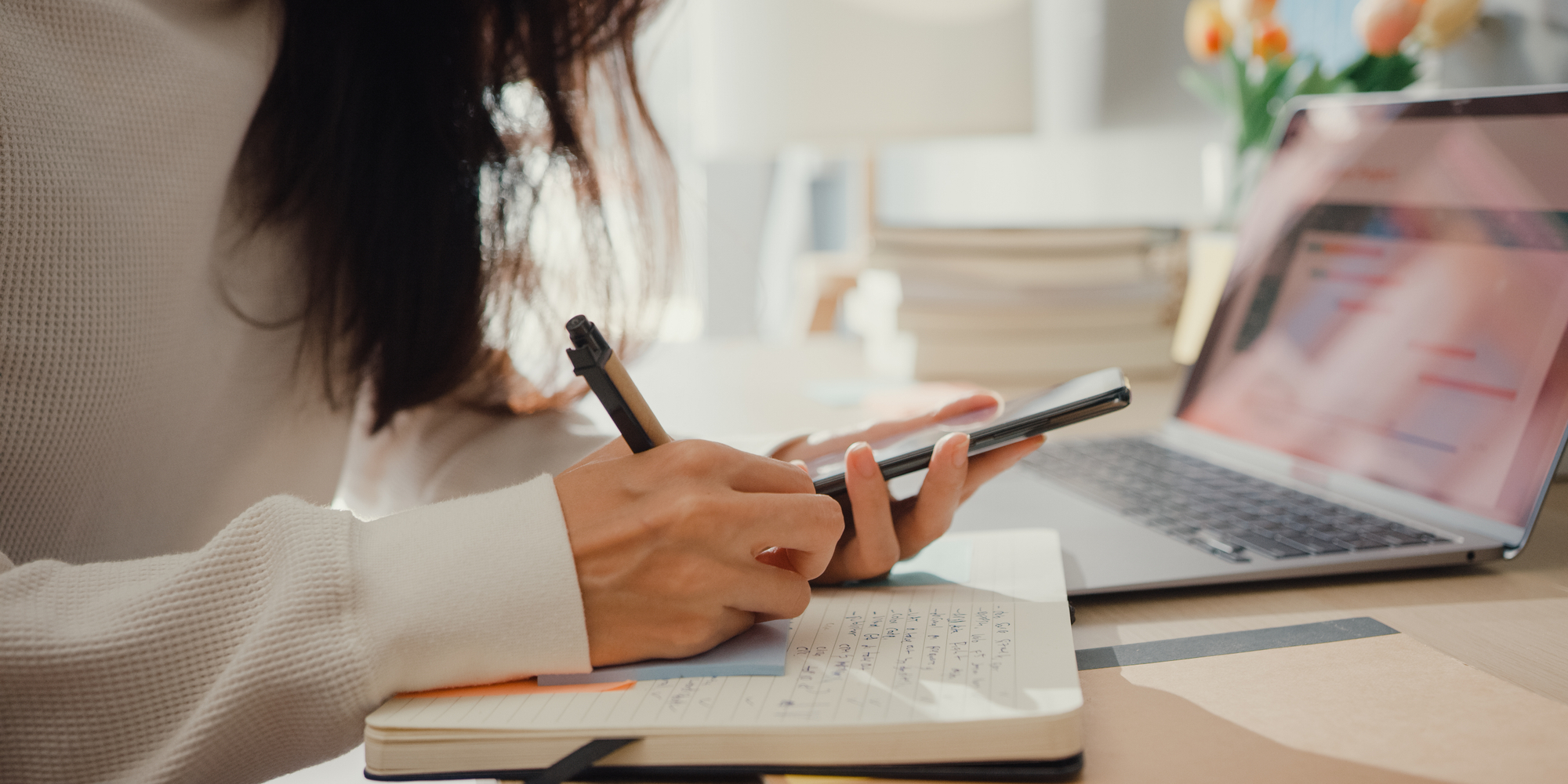 Woman using her phone and writing in a notebook