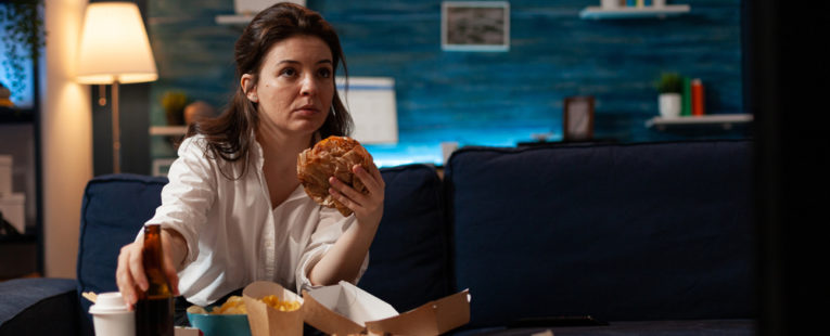 Stock of female eating unhealthy food on couch