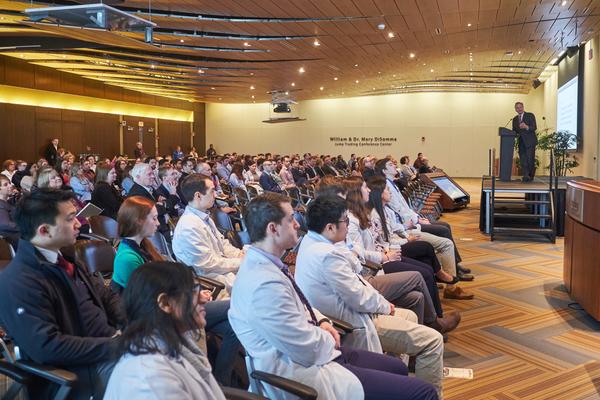 Large clinical crowd listens to speaker at stage