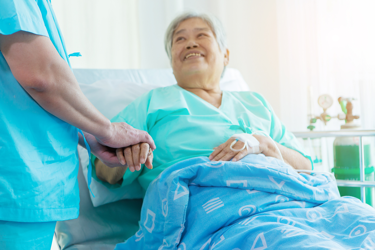 Female Patient in Hospital Gown Holds Hand of Provider