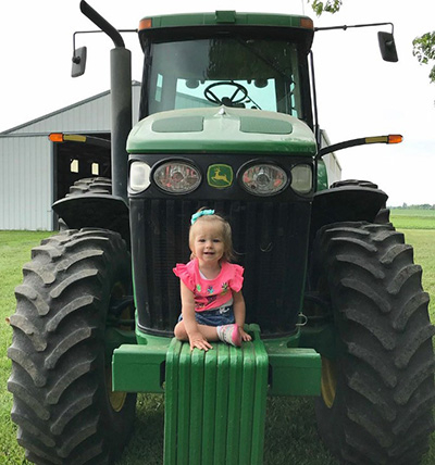 A cheerful Adalie Guth sits on a tractor on her family farm.