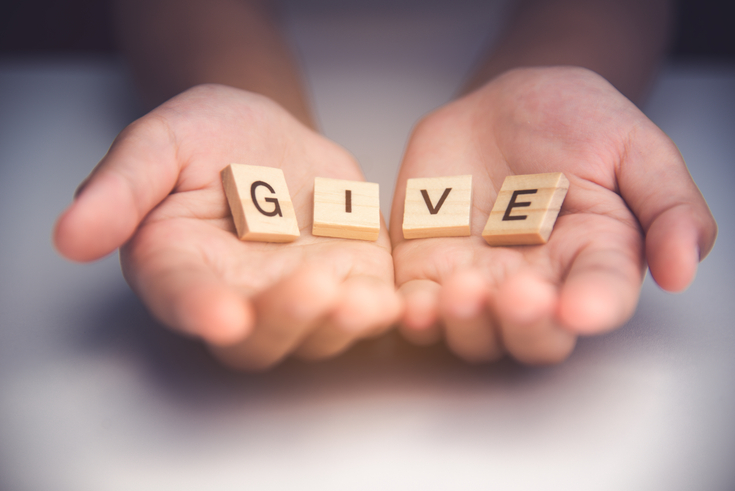 Close-up of two cupped hands holding wooden blocks that spell out the word "GIVE" against a soft, neutral background.